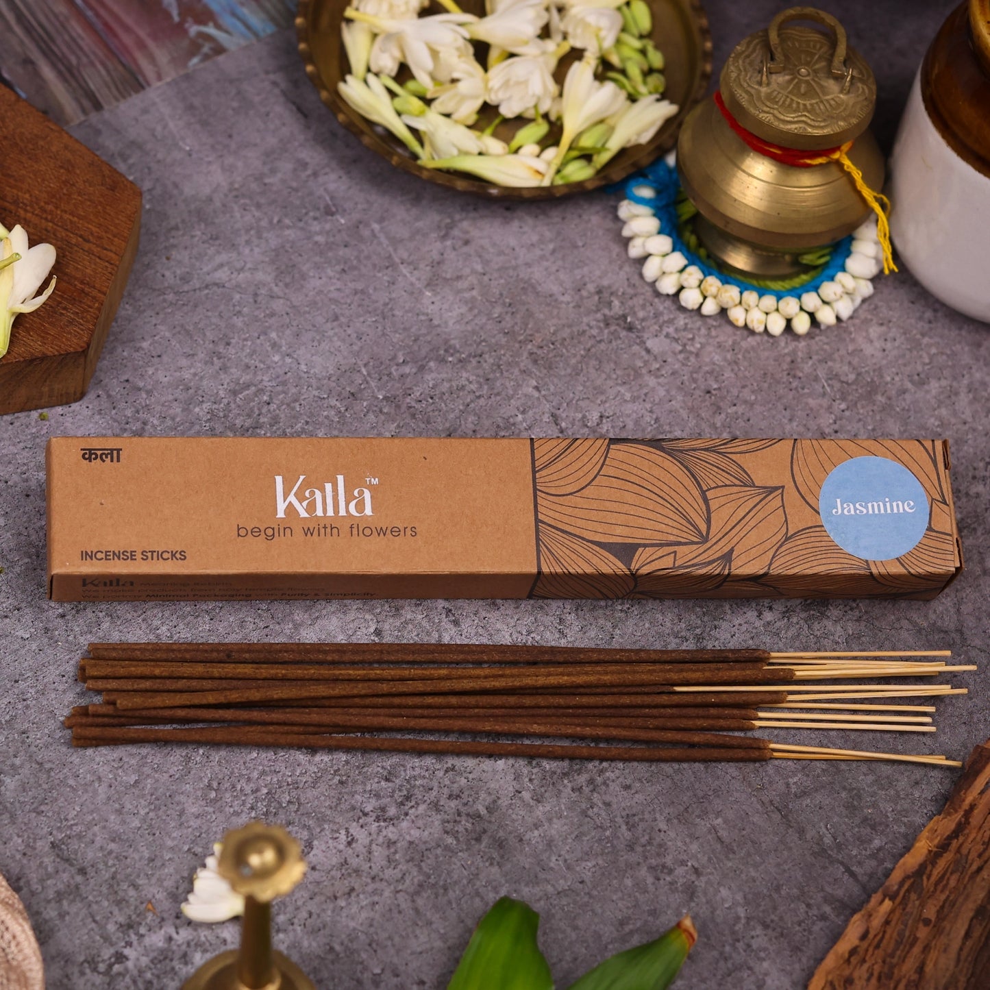 Kalla Jasmine Incense Sticks – natural brown packaging with elegant leaf illustrations and a soft blue label marked “Jasmine,” displayed on a stone surface surrounded by jasmine flowers, brass decor, and incense sticks for a serene, floral-themed ambiance.