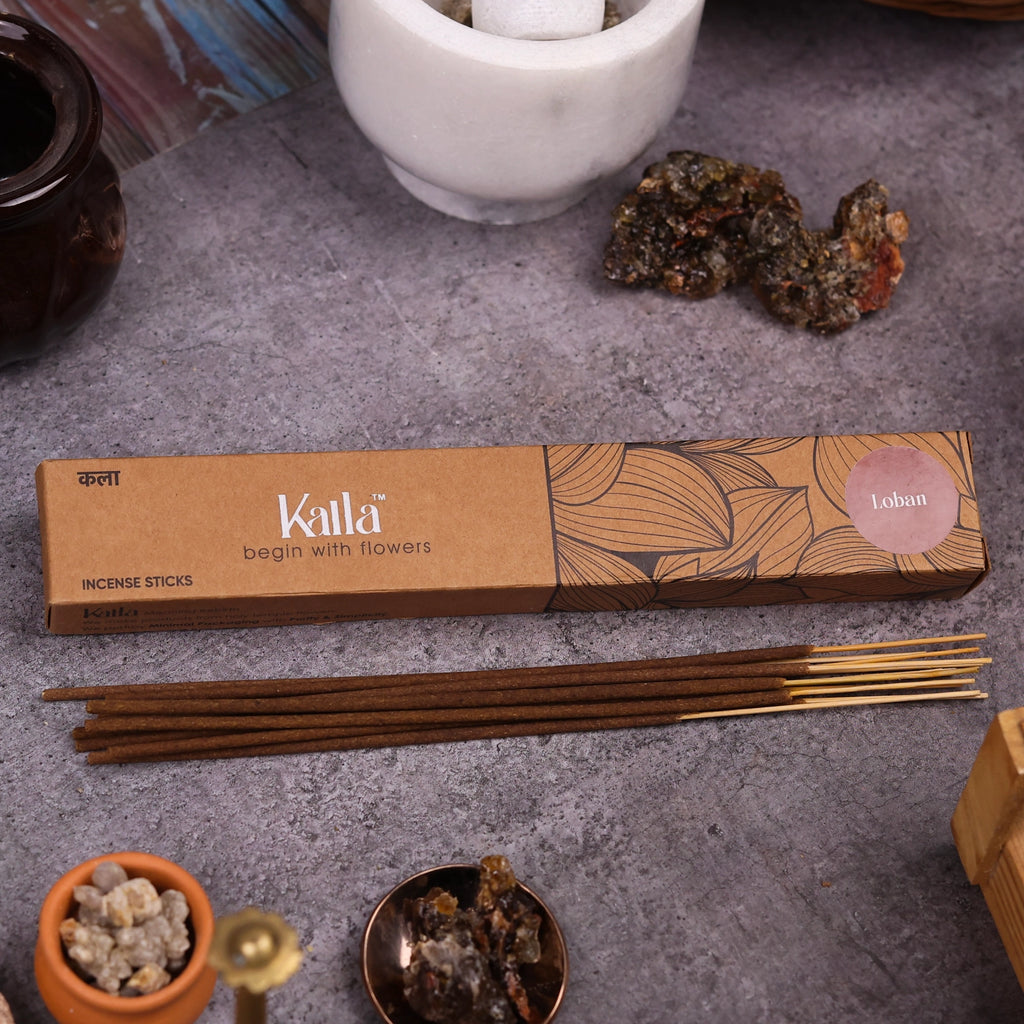 Kalla Loban Incense Sticks – earthy brown packaging with artistic leaf illustrations and a muted mauve label reading “Loban,” displayed on a stone background with aromatic resin pieces, brass decor, and incense sticks for a warm, traditional ambiance.