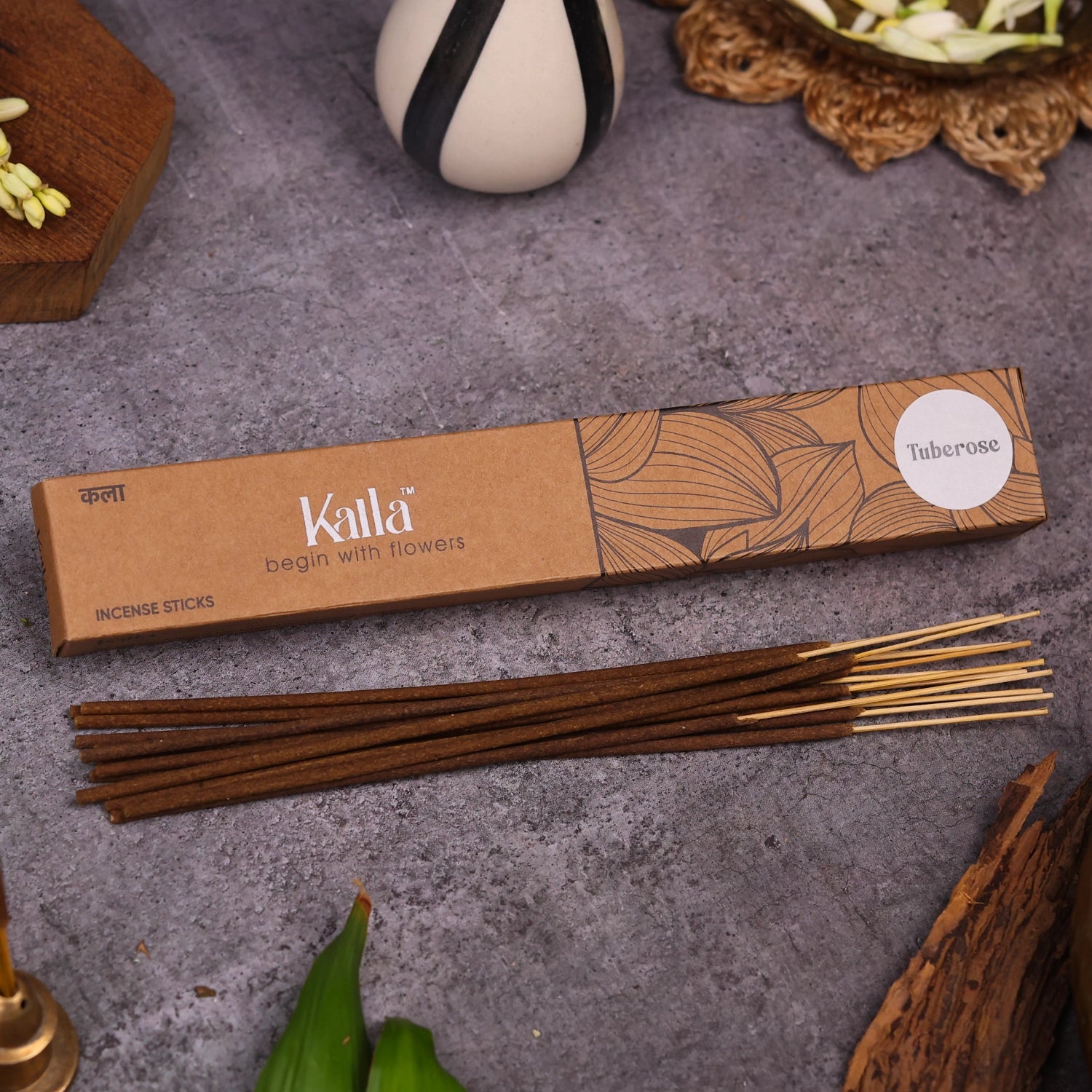 Kalla Tuberose Incense Sticks – eco-friendly brown packaging with artistic floral line designs and a white label marked “Tuberose,” displayed on a textured grey surface with incense sticks arranged neatly, surrounded by natural decorative elements for a serene and floral ambiance.