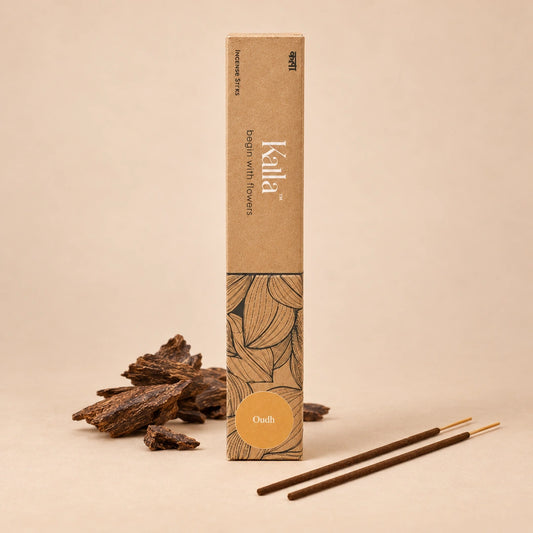 Kalla Oudh incense sticks placed on a stone surface alongside the product's eco-friendly packaging. Decorative elements like brass spoons with resin, a marble mortar and pestle, and other natural ingredients surround the setup, evoking a sense of calm and luxury.
