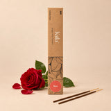 Kalla Rose Incense Sticks – natural brown packaging with elegant floral line patterns and a red label marked “Rose,” displayed on a grey stone surface with incense sticks spread out, surrounded by red rose petals and decorative elements for a calming, aromatic setting.