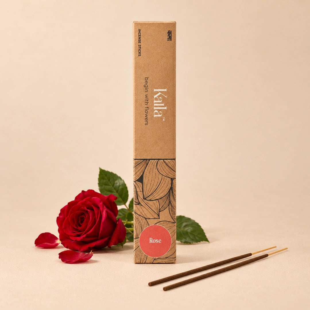 Kalla Rose Incense Sticks – natural brown packaging with elegant floral line patterns and a red label marked “Rose,” displayed on a grey stone surface with incense sticks spread out, surrounded by red rose petals and decorative elements for a calming, aromatic setting.