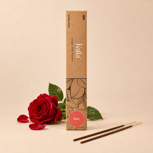 Kalla Rose Incense Sticks – natural brown packaging with elegant floral line patterns and a red label marked “Rose,” displayed on a grey stone surface with incense sticks spread out, surrounded by red rose petals and decorative elements for a calming, aromatic setting.